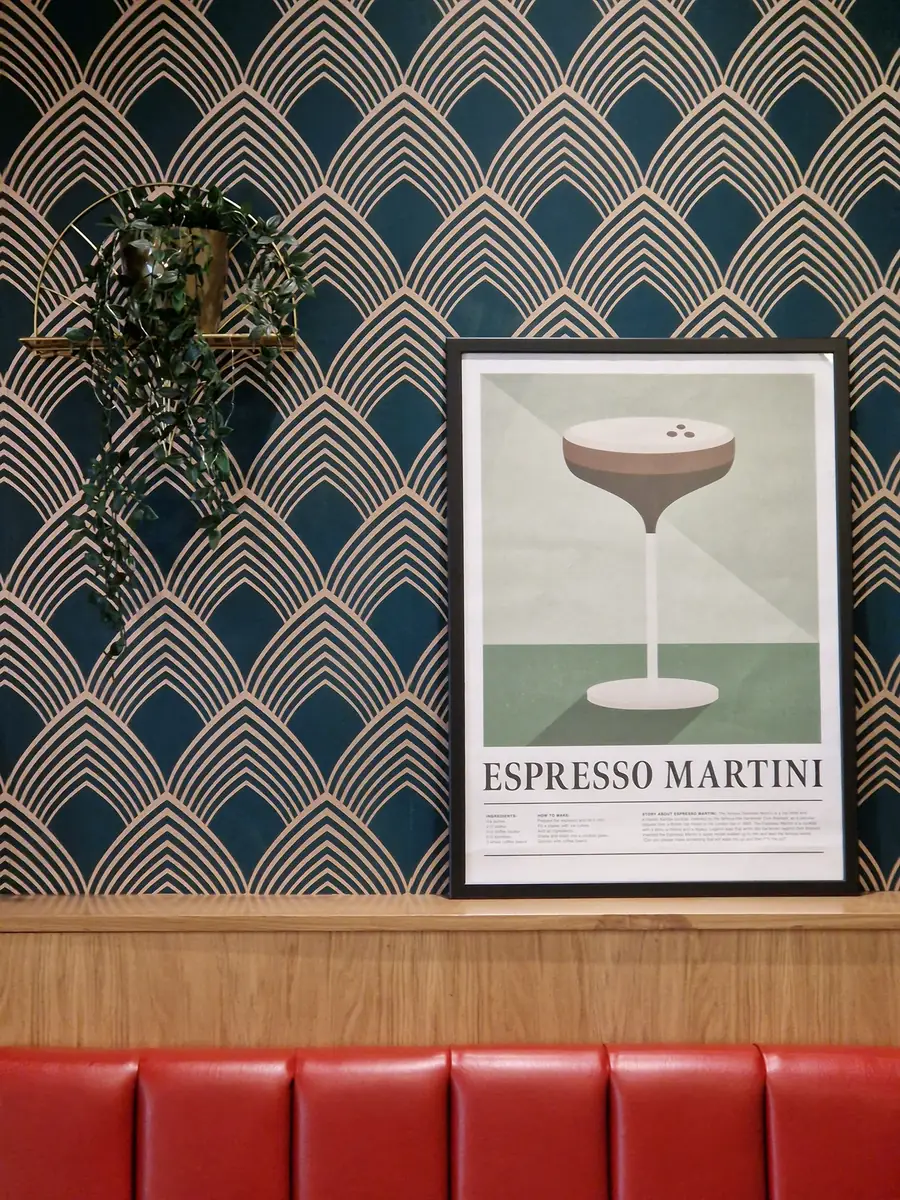 Deco fan wallpaper in teal and blush with a brass shelf and a red leather banquette.