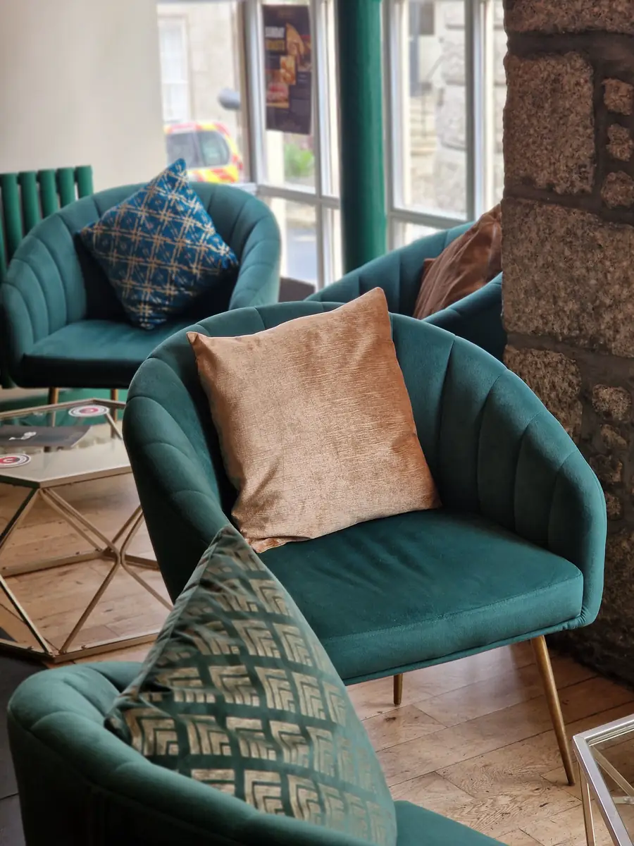 Teal velvet tub chairs with brass legs beside a bare granite wall.